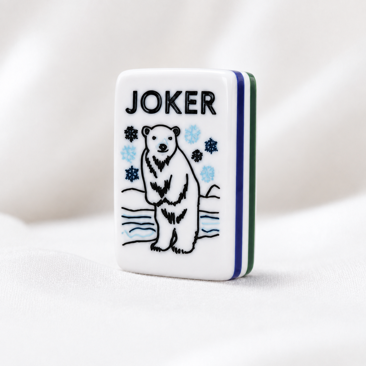 Close-up of polar bear Joker mahjong tile with blue and black snowflakes and blue green striped sides.