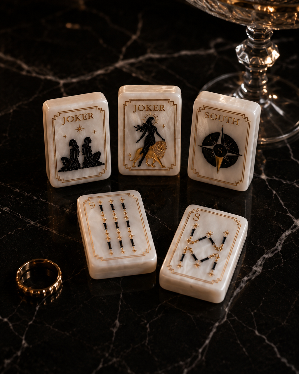 Luxury black and gold Mahjong tiles displayed on dark marble beside crystal glassware
