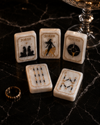 Luxury black and gold Mahjong tiles displayed on dark marble beside crystal glassware