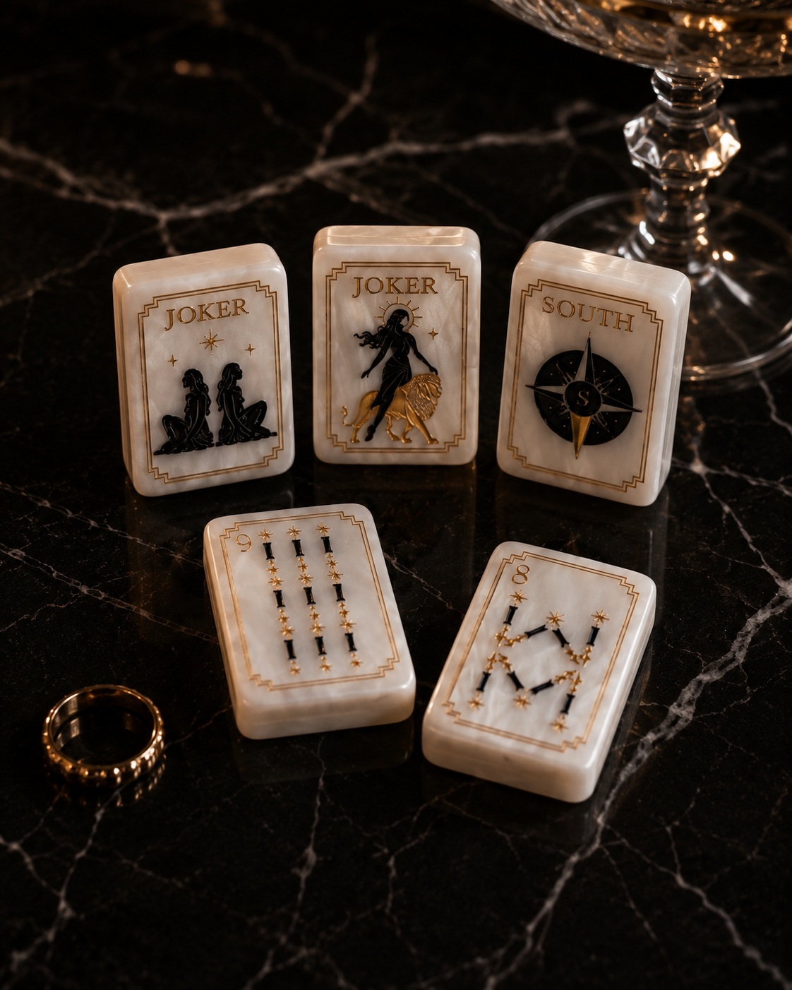 Luxury black and gold Mahjong tiles displayed on dark marble beside crystal glassware