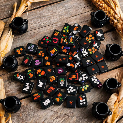 Black Halloween mahjong tiles with colorful ghost, pumpkin, skull and spooky designs scattered on a rustic wooden table.