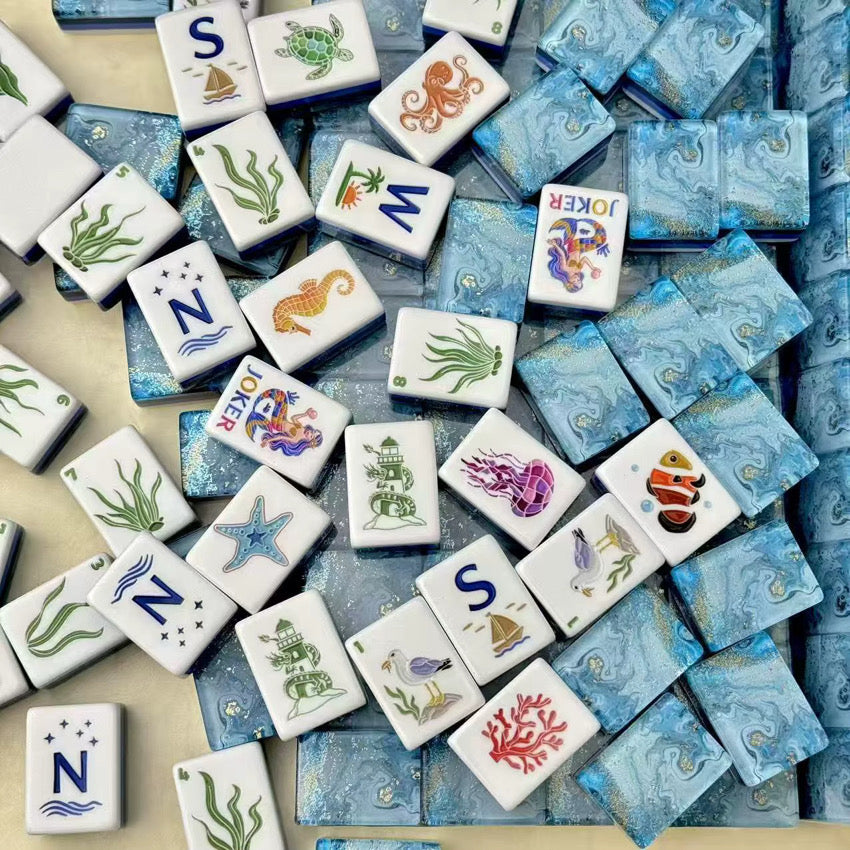 Ocean-themed mahjong tiles scattered across a light surface, featuring colorful sea-life illustrations and blue marbled backs.