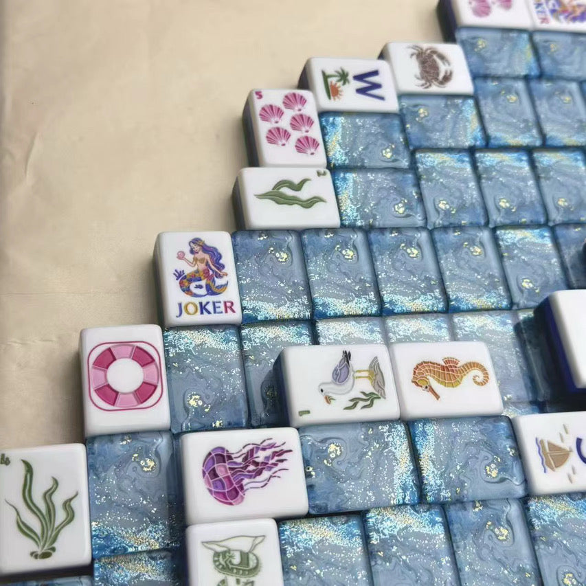 Partially arranged ocean-themed mahjong game with blue marbled tiles and illustrated sea-creature tiles on a beige table.
