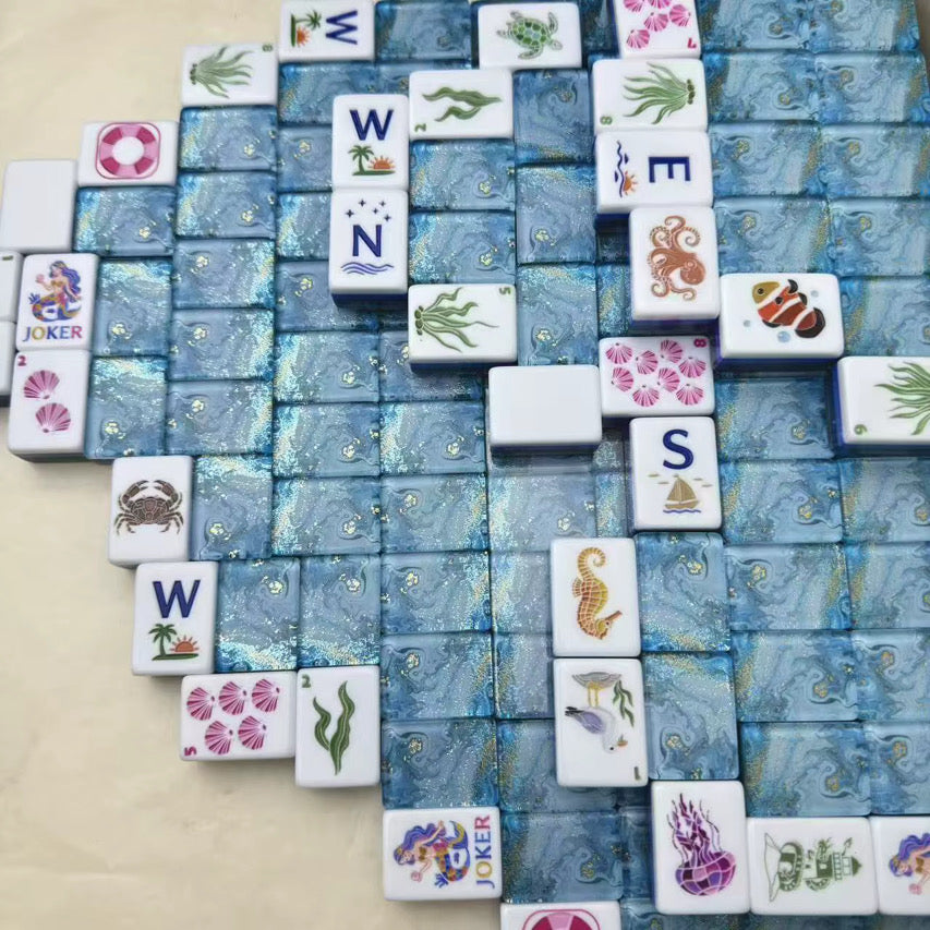 Ocean-themed mahjong tiles arranged in a square game layout with blue marbled backs and colorful nautical illustrations.
