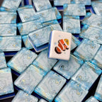 Clownfish mahjong tile displayed upright on a pile of glossy blue marbled tiles.