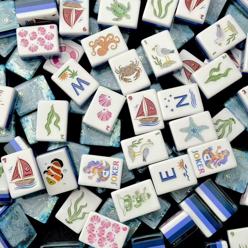 Colorful ocean-inspired mahjong tiles scattered on a dark background, showing sea creatures, sailboats, winds, and Jokers.