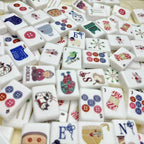 Overhead view of a white knitting-themed mahjong set with cats, yarn, buttons, birds, and cozy craft illustrations