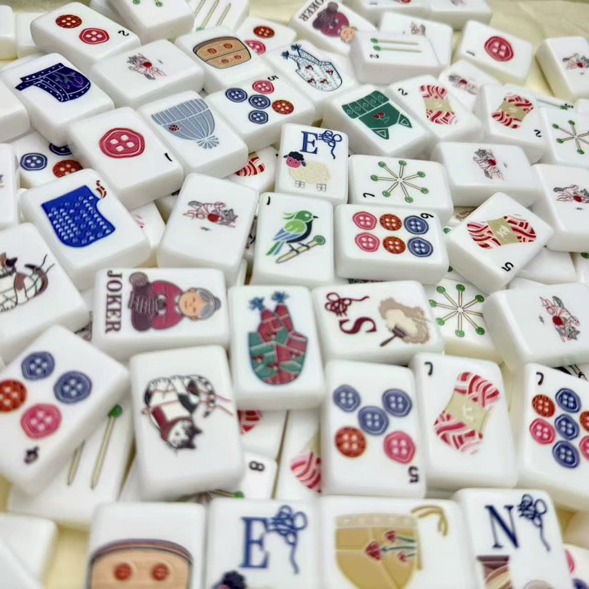 Overhead view of a white knitting-themed mahjong set with cats, yarn, buttons, birds, and cozy craft illustrations