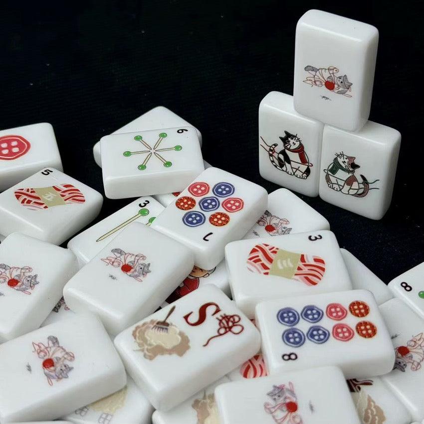 White knitting-themed mahjong tiles scattered on a black background with three illustrated cat tiles stacked upright