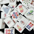 Close-up of glossy white mahjong tiles with cat, knit hat, yarn, bird, and colorful button illustrations