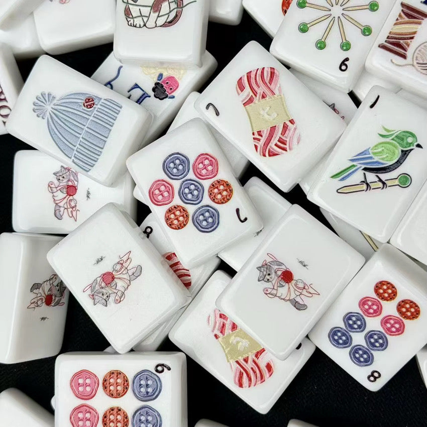 Close-up of glossy white mahjong tiles with cat, knit hat, yarn, bird, and colorful button illustrations